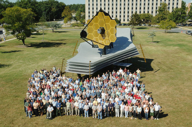 NASA/Goddard Space Flight Center/Pat Izzo's photo: The Webb Telescope team posing with the full-scale model of the James Webb Space Telescope on the lawn at Goddard Space Flight Center, where it was displayed September 19-25, 2005. (September 2005) via Wikimedia Commons, used w/o permission.